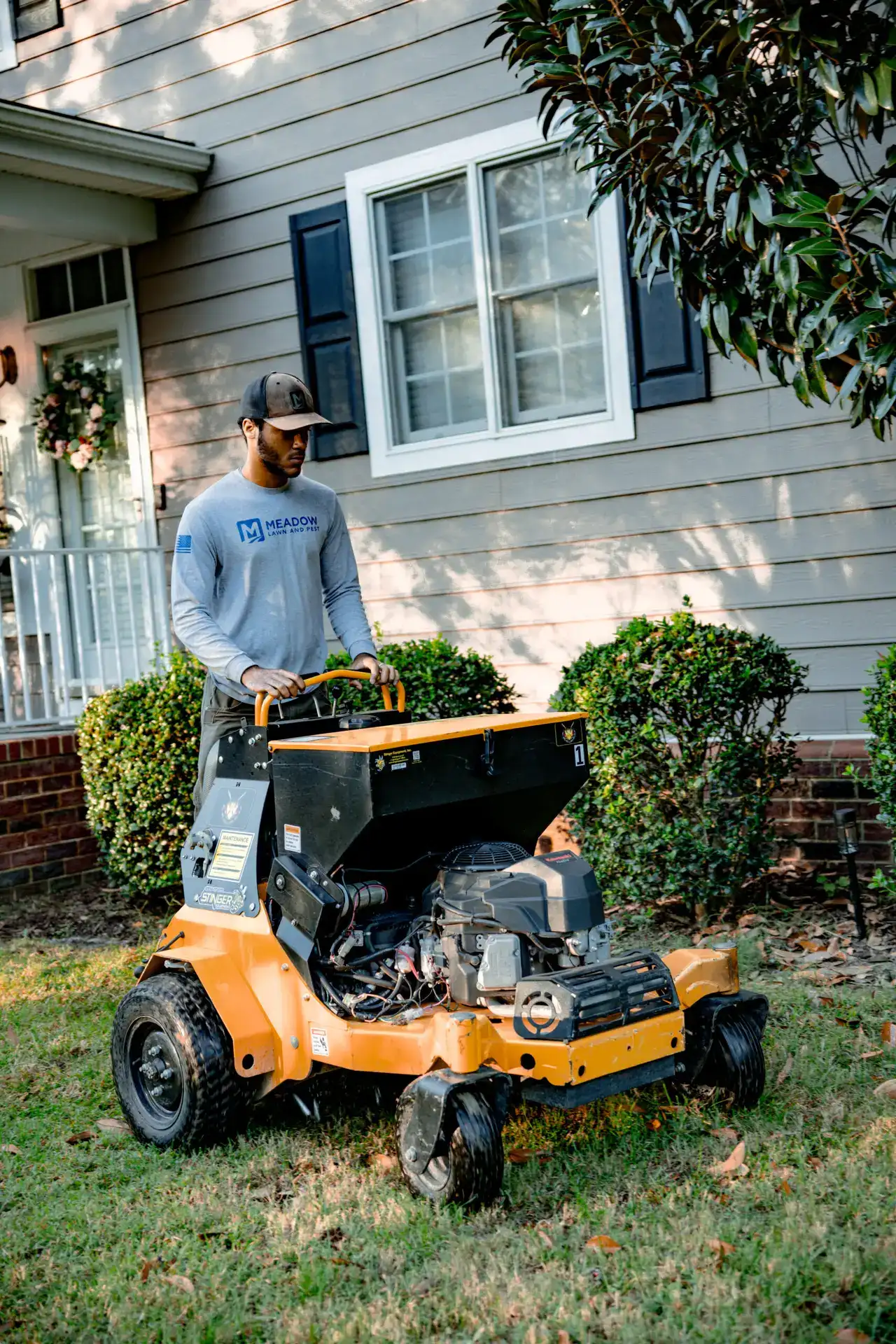 Meadow Lawn & Pest technician applying lawn fertilizer with a stand-on spreader outside a Newport News home