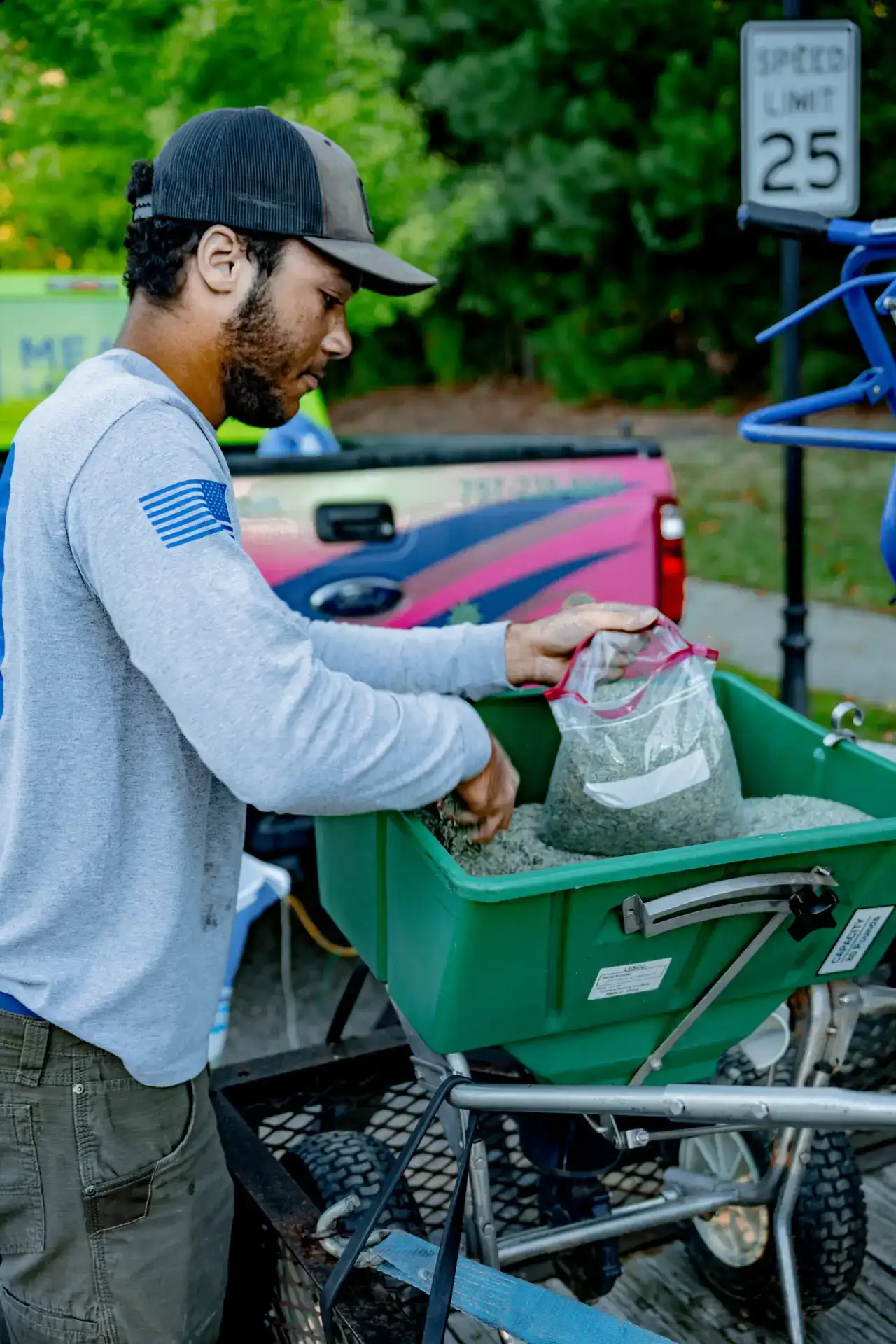 Lawn care technician filling a Lesco broadcast spreader with granular fertilizer in Newport News